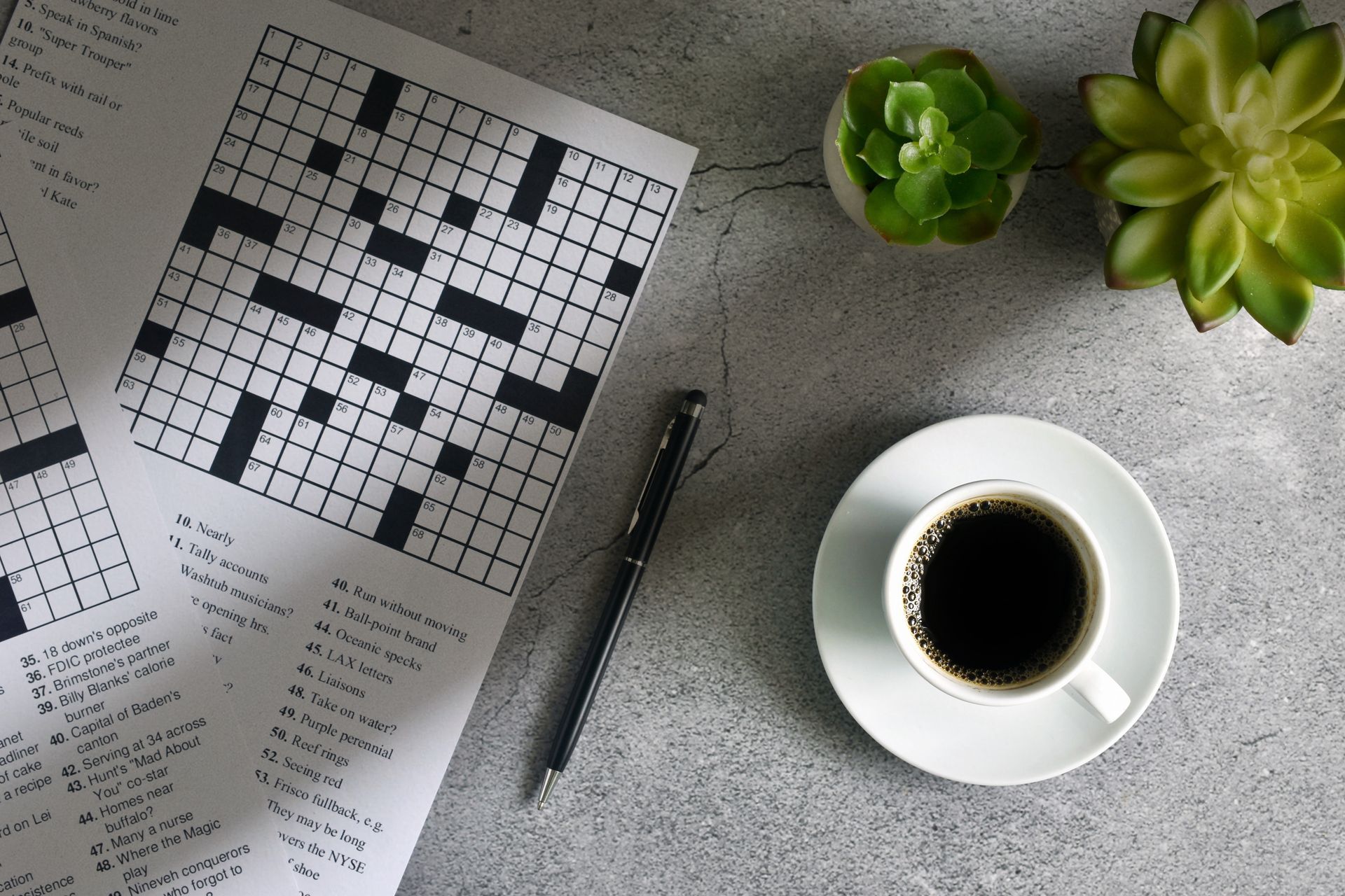 mesa com revista de palavras cruzadas, com uma xícara de café e uma caneta