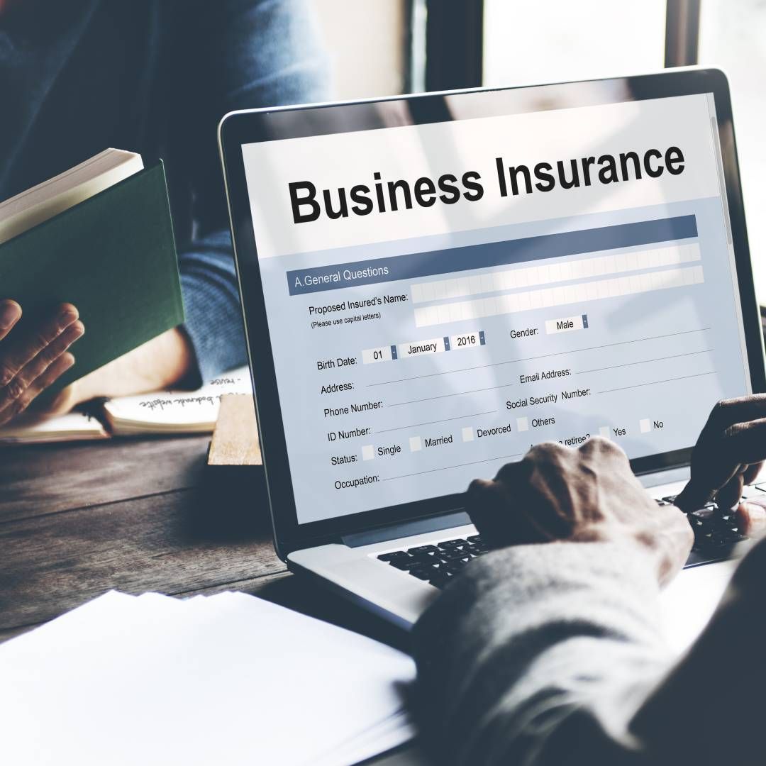 A person is typing on a laptop that says business insurance on the screen