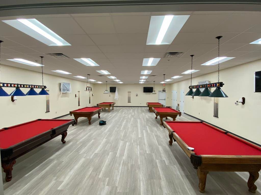 A billiards room with several red-felted pool tables, overhead lighting, and pendant lamps.