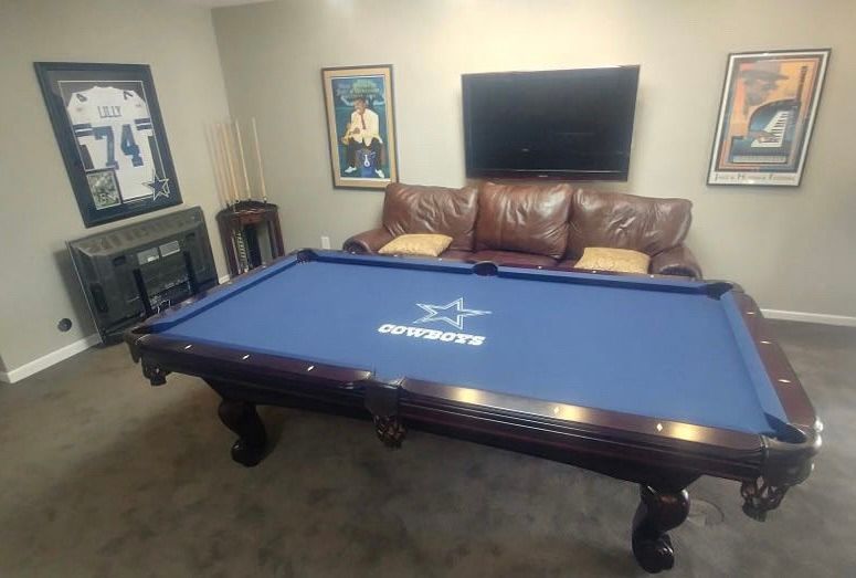 Blue felt pool table with Dallas Cowboys logo, sofa, and TV in a game room.