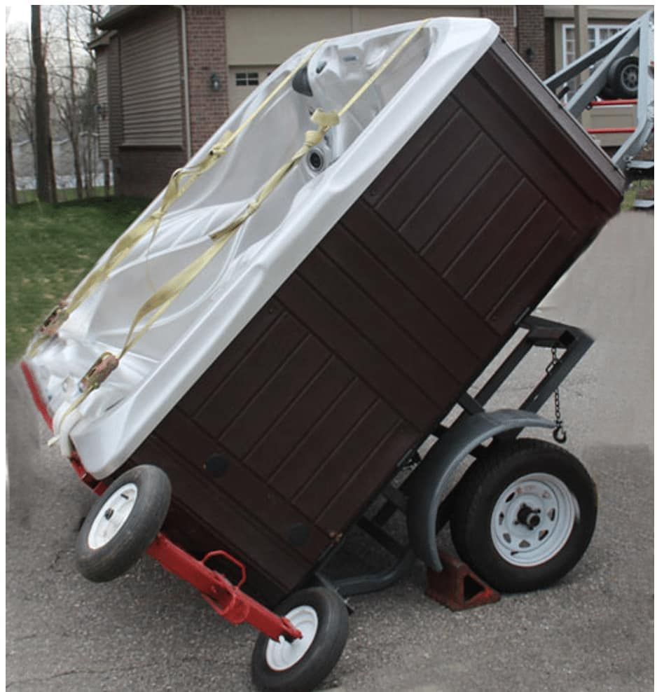 A hot tub secured on a tilted trailer, on asphalt, in front of a house.