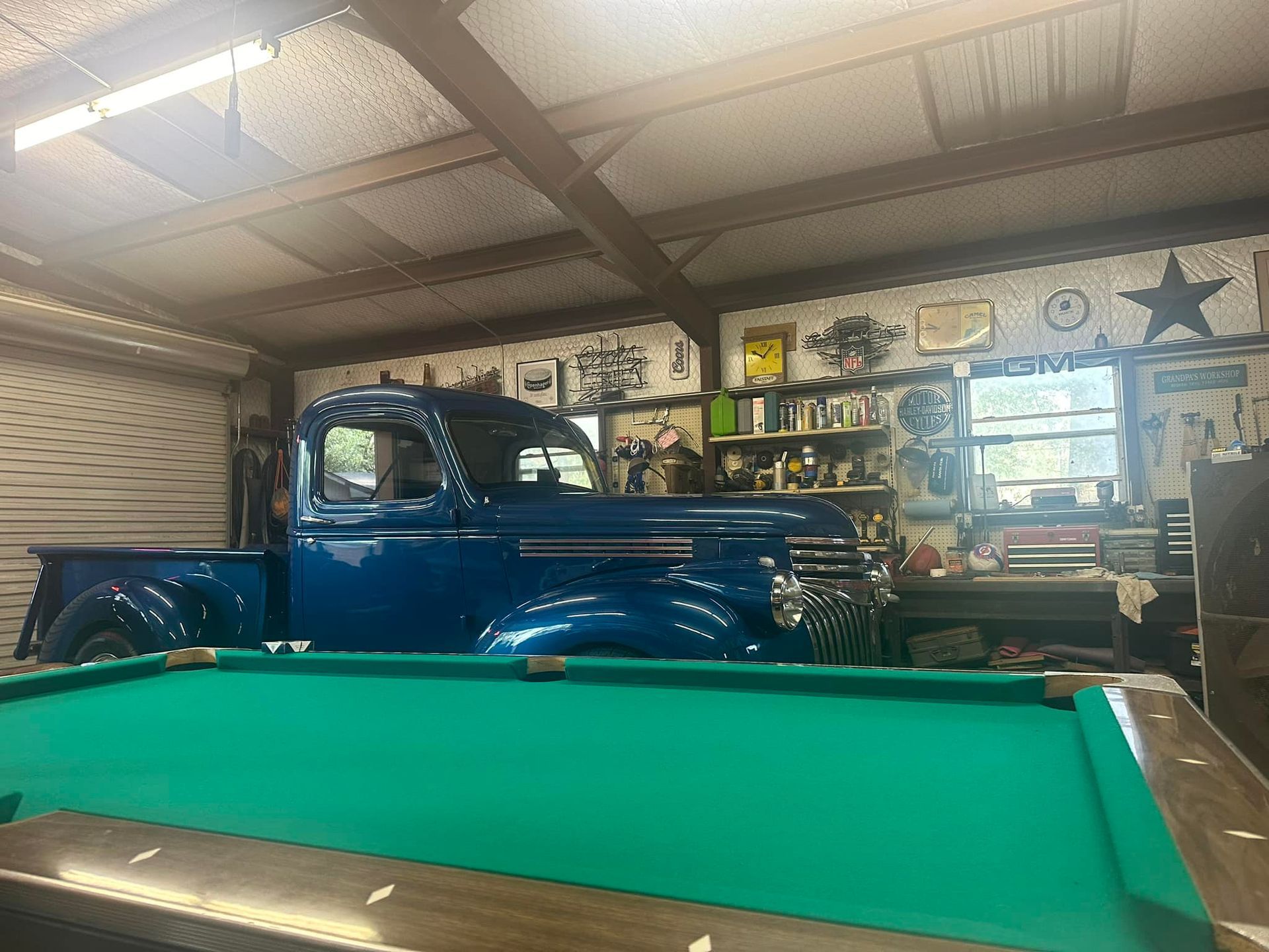 Blue classic truck parked inside a garage next to a pool table.