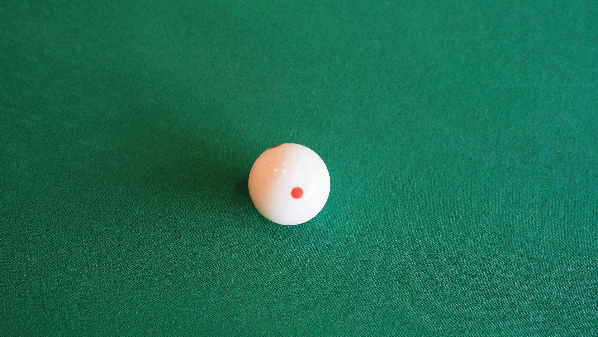 White cue ball with red dot on a green pool table.