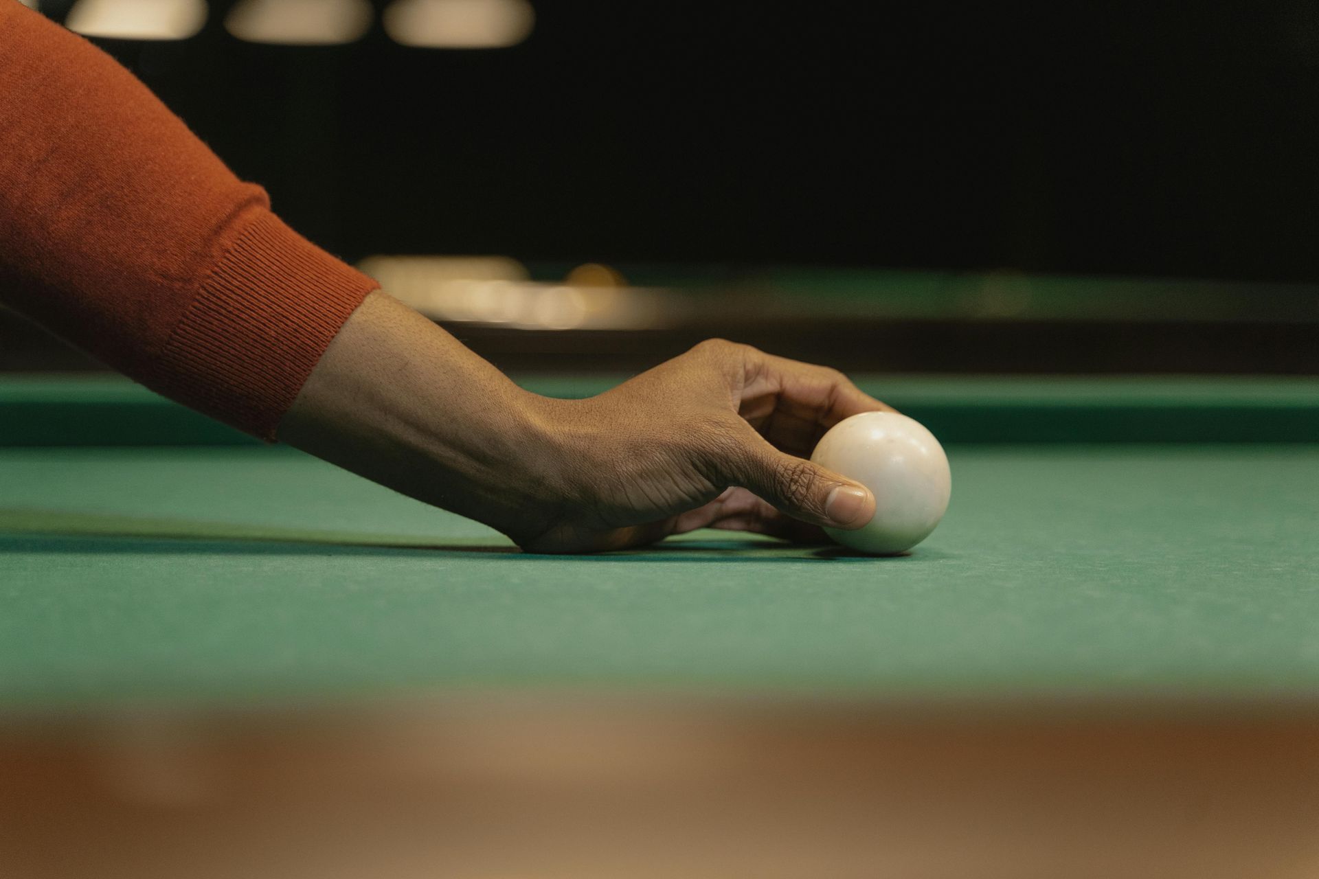 Hand placing a white cue ball on a green pool table.