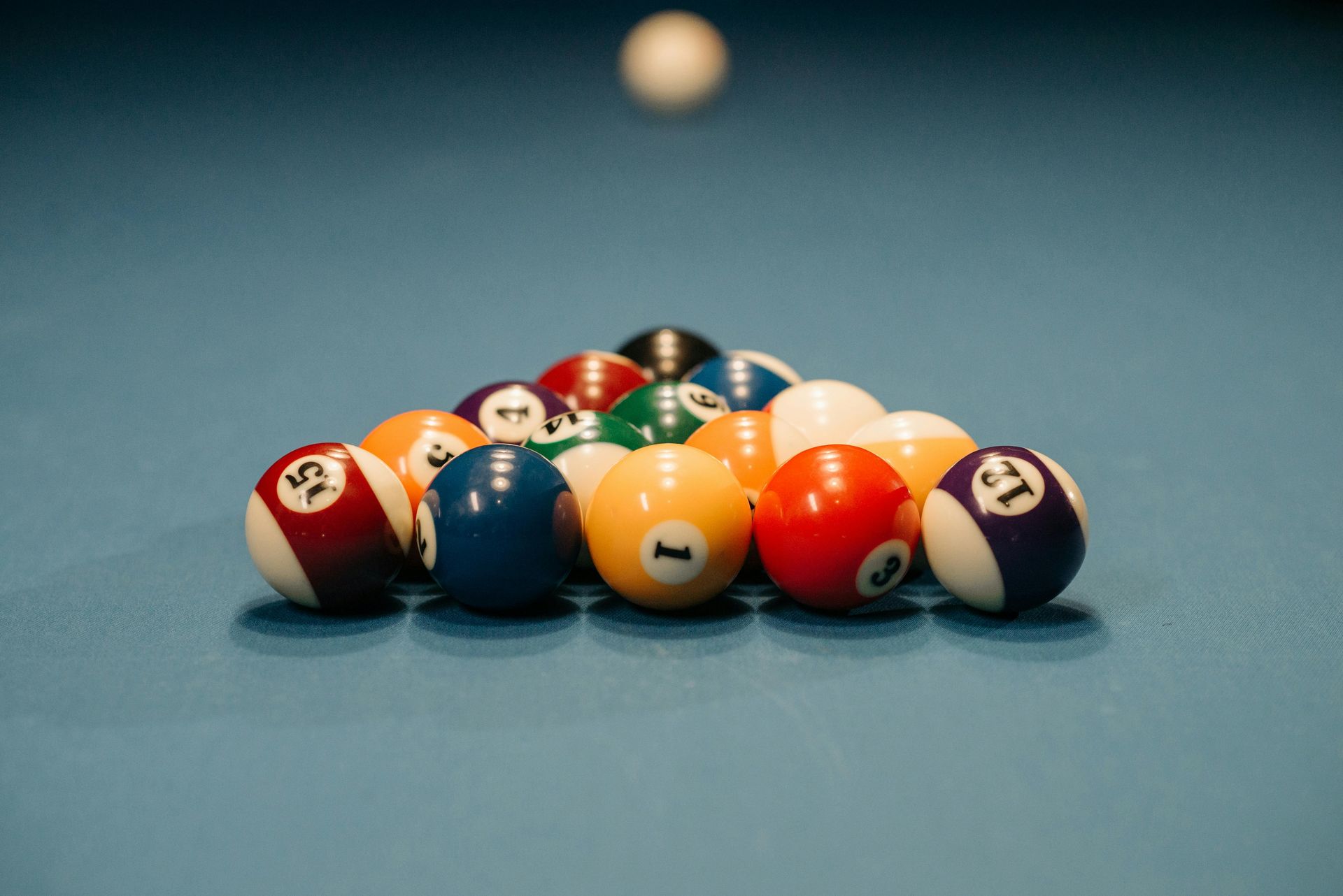 Pool balls racked on a blue felt table, cue ball above.