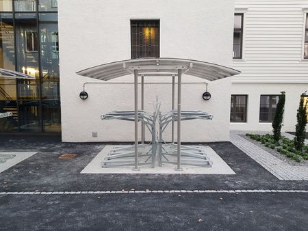 Folk sykler og går langs et fortau med trær. Sykler parkert i stativ.