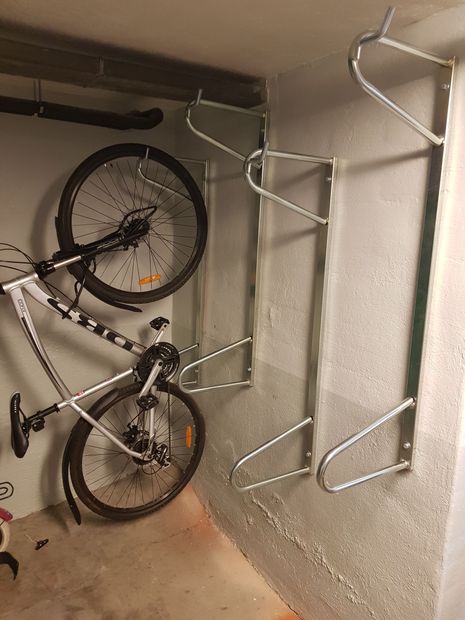 Sykkelskur med sykler parkert inne, foran en bygård, på en solskinnsdag.