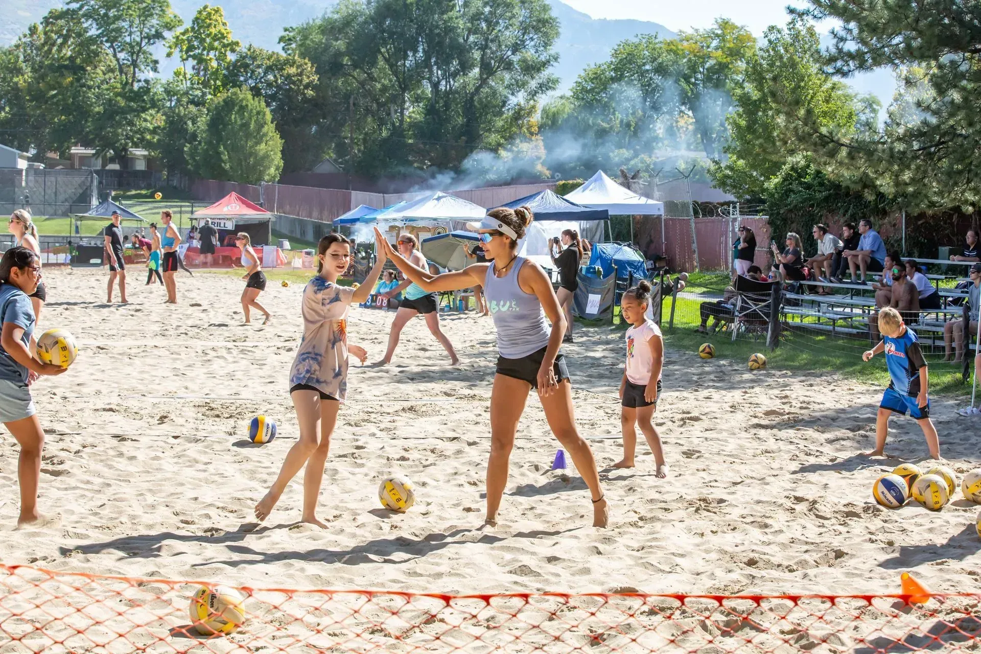 Six women pose on podiums holding volleyballs on a sand court.