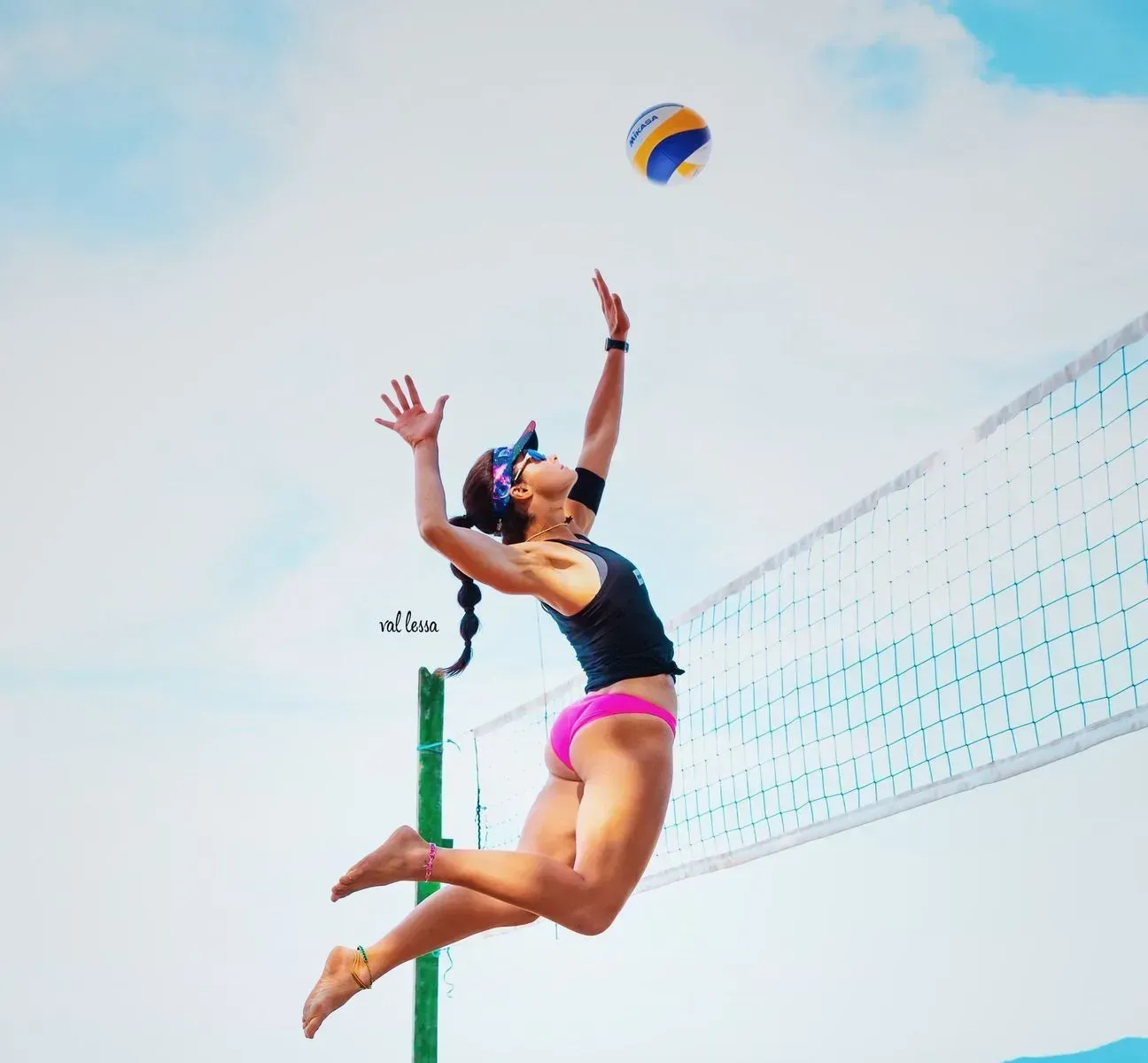 Woman in pink bikini spikes volleyball on a beach.