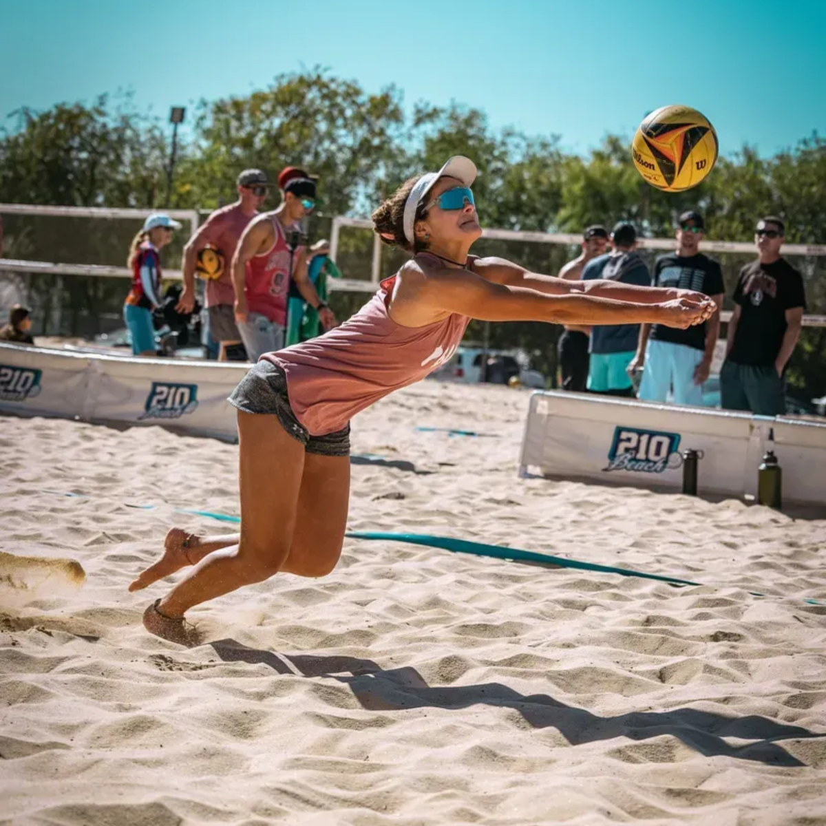Woman diving to play beach volleyball in the sand.