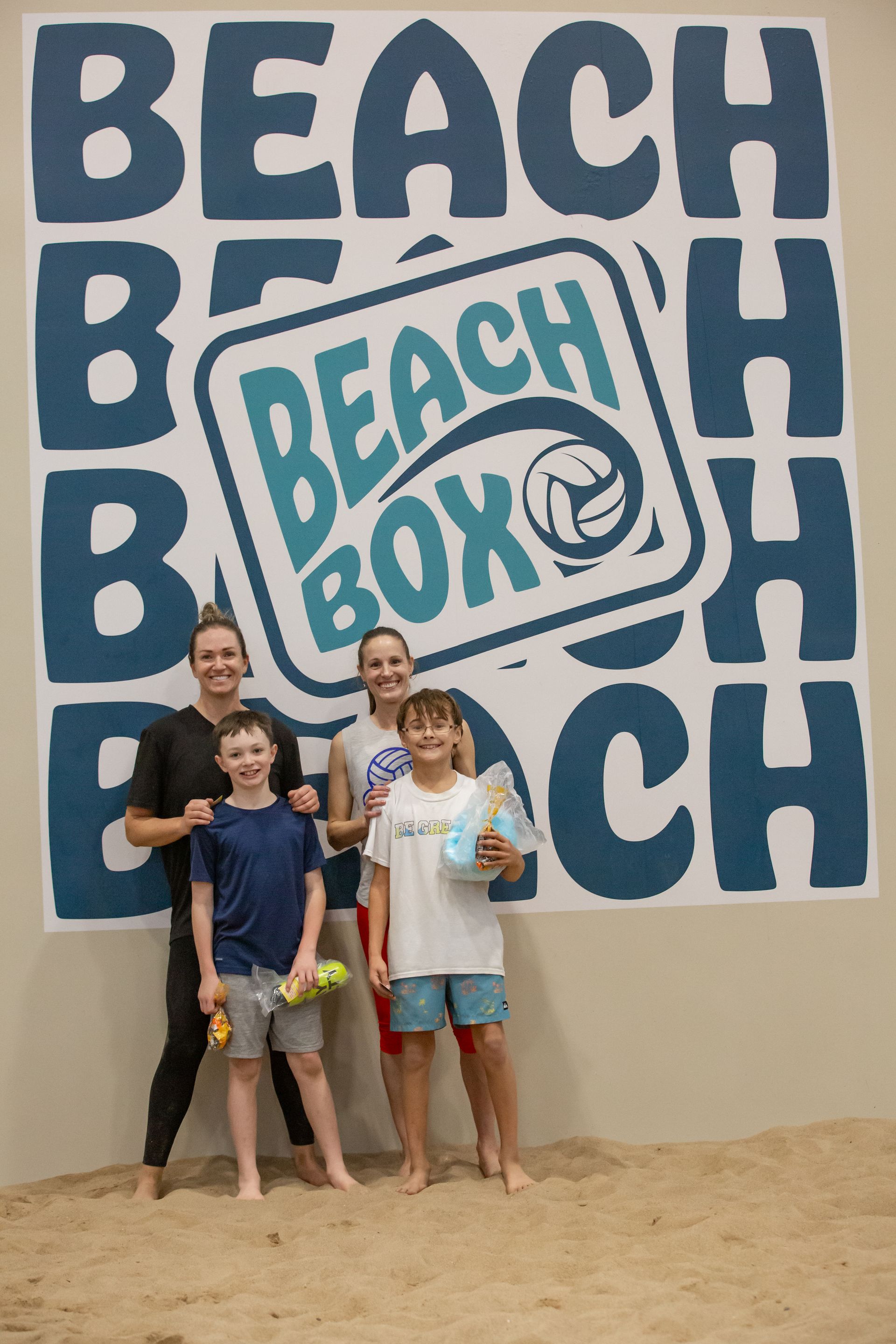 Six women pose on podiums holding volleyballs on a sand court.