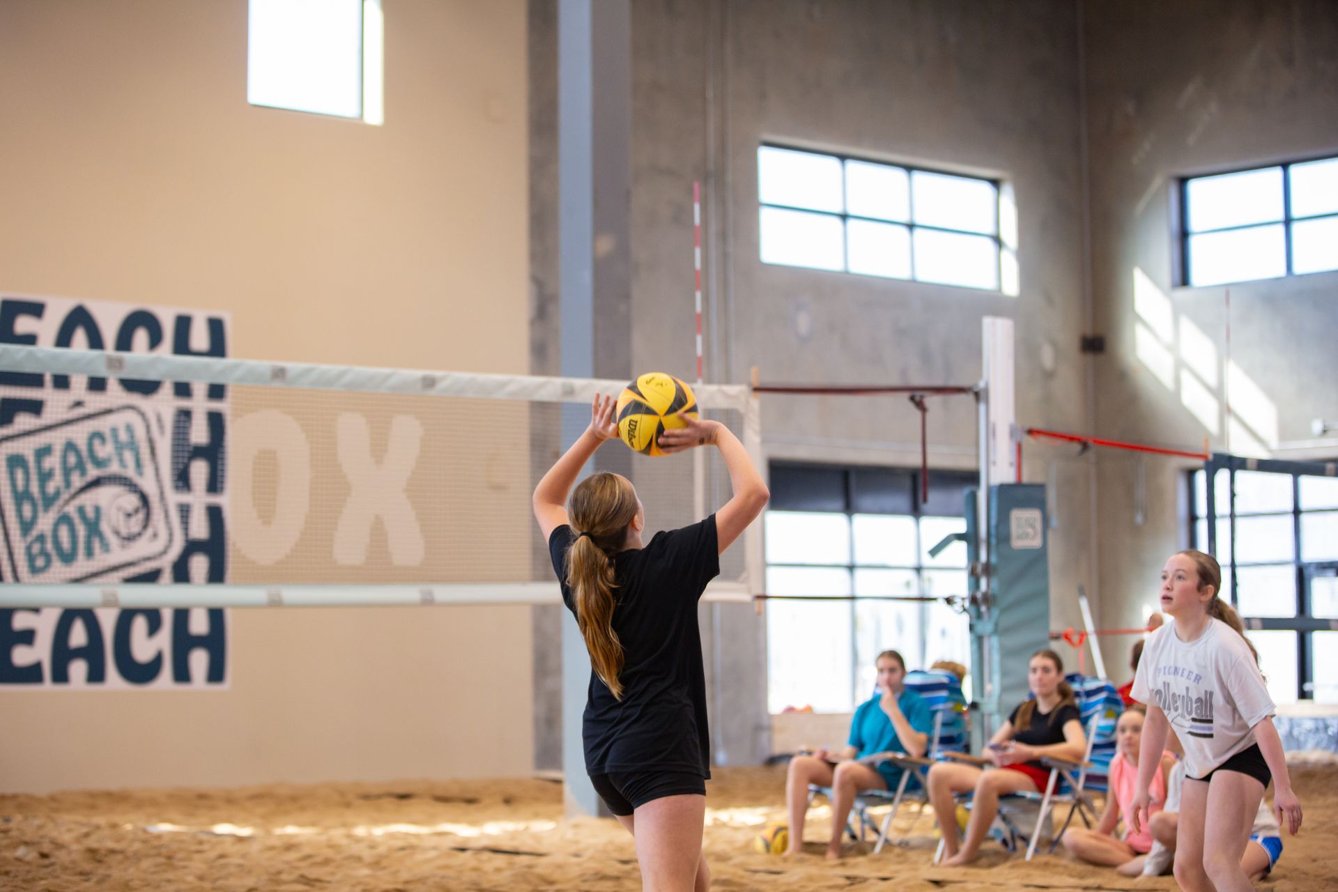 Woman playing with a volleyball on sand, wearing a pink sweatsuit. 