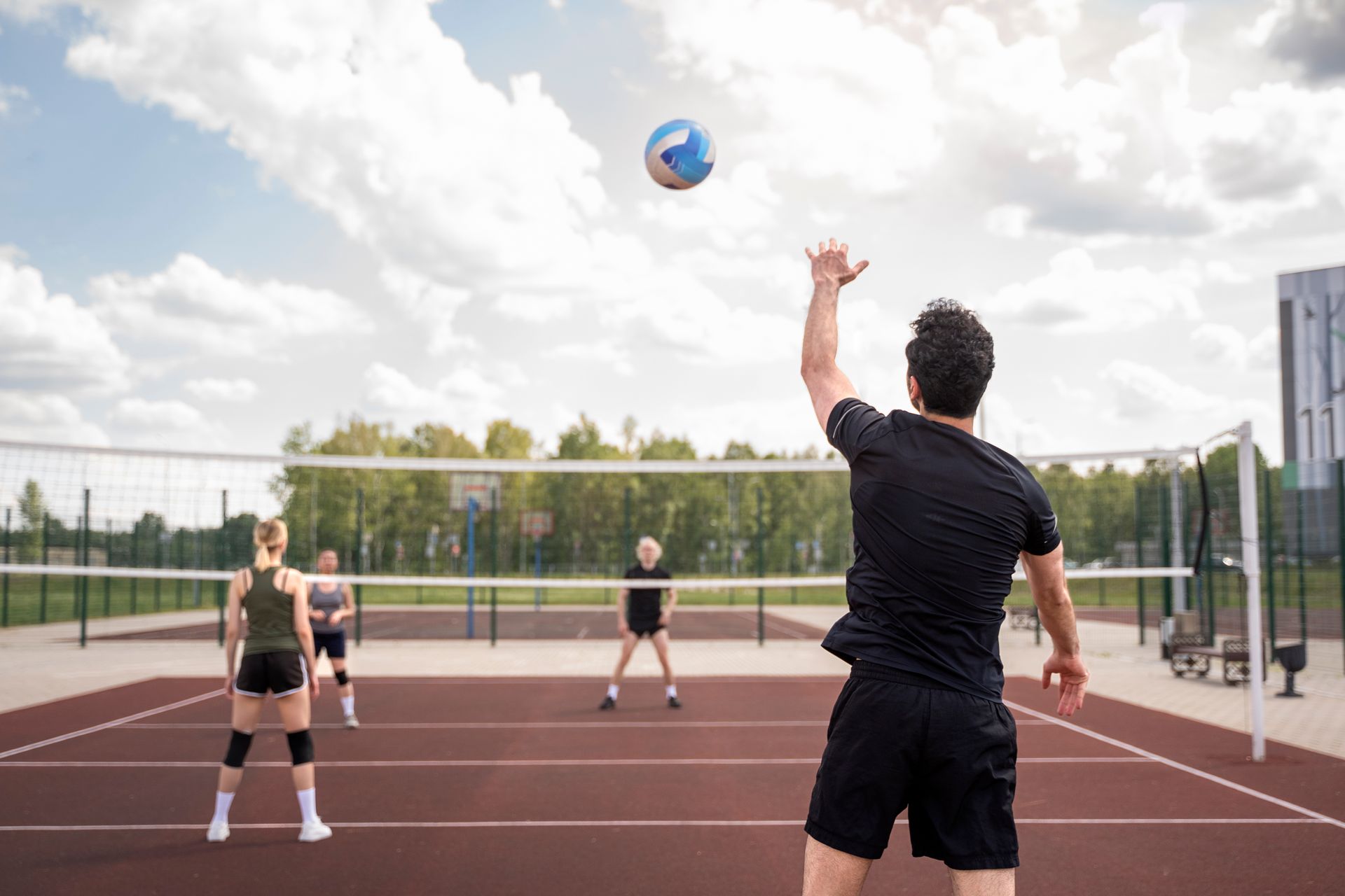 Woman bouncing a yellow and black ball, wearing a pink sweatsuit on a sand court. A sign reads Woman bouncing a yellow and black ball, wearing a pink sweatsuit on a sand court. A sign reads