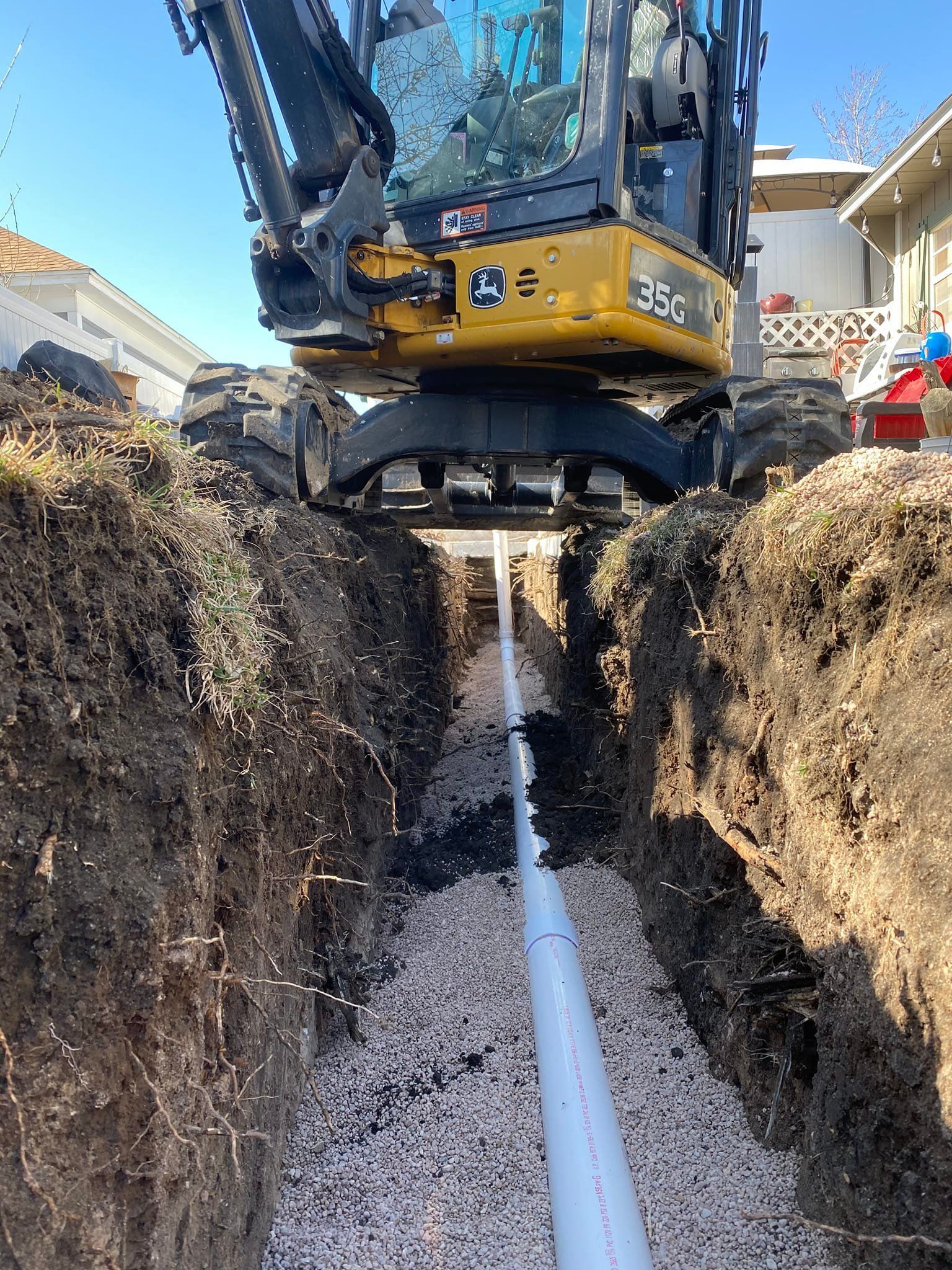 A yellow and black excavator is digging a trench with a pipe in it.