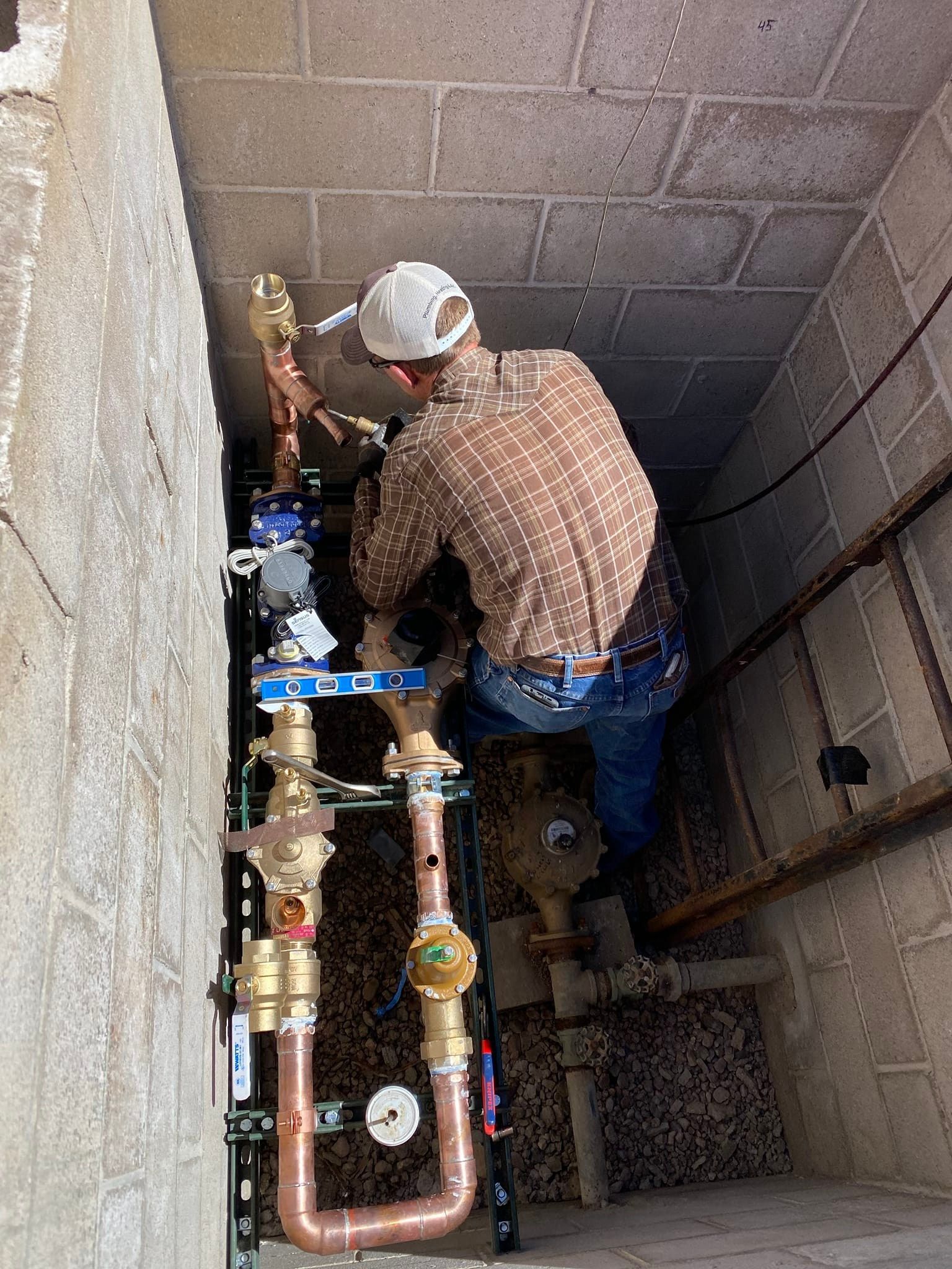 A man is working on a water meter in a basement.