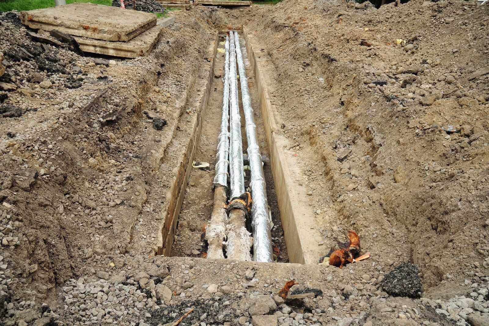 A bunch of pipes are laying in the dirt in a trench.