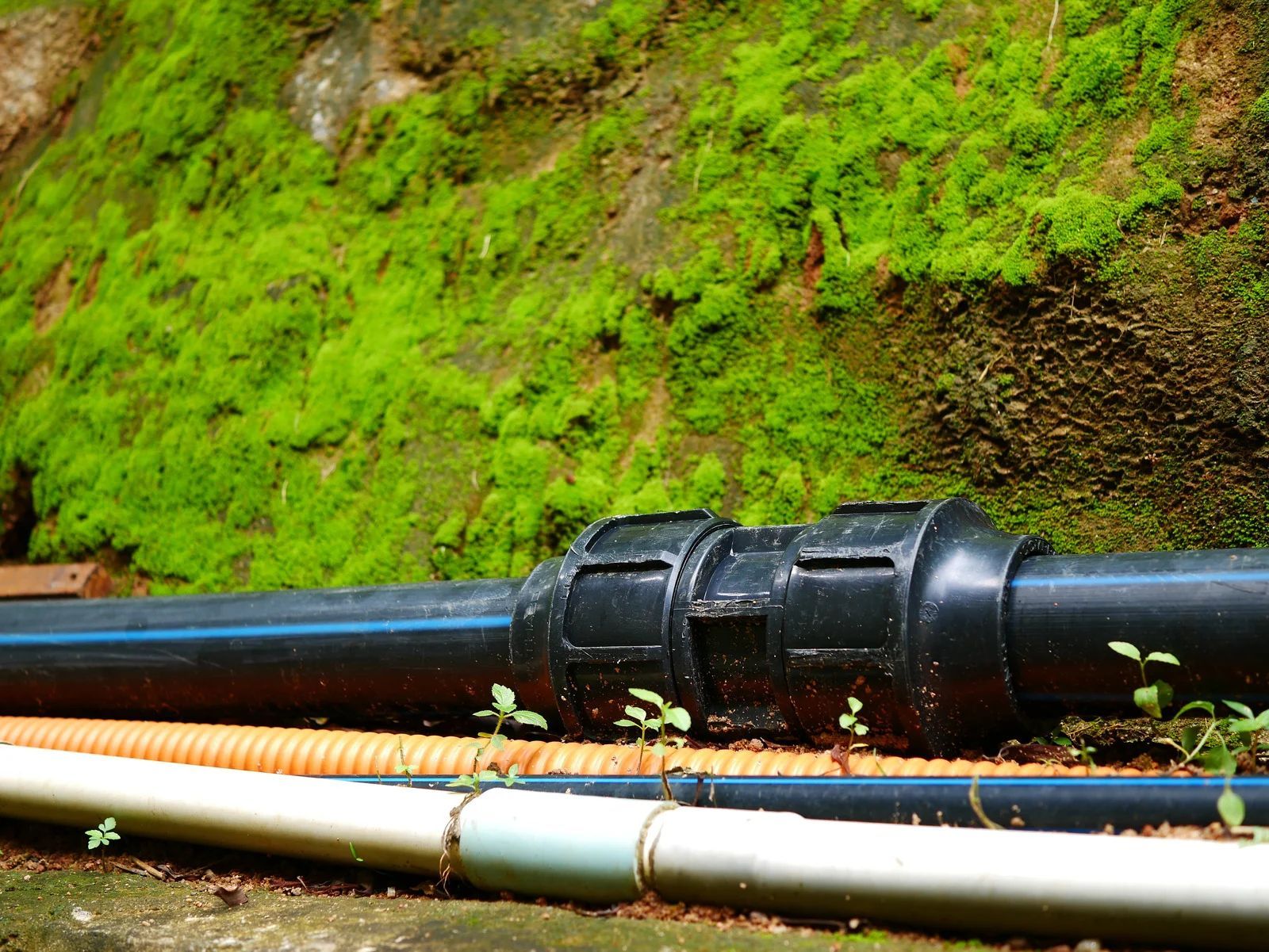 Black pipes connected with a coupling, against a mossy rock wall.