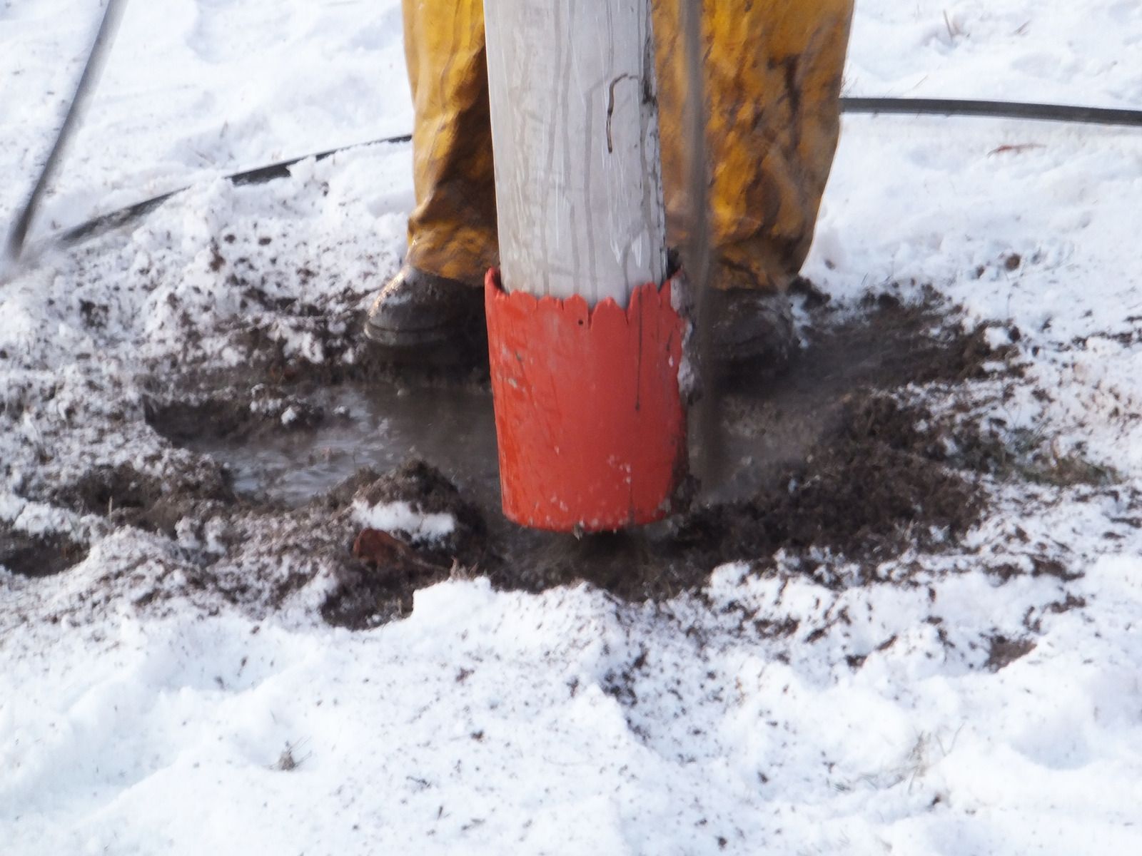 Red-tipped wooden post planted in snow with muddy ground around its base.