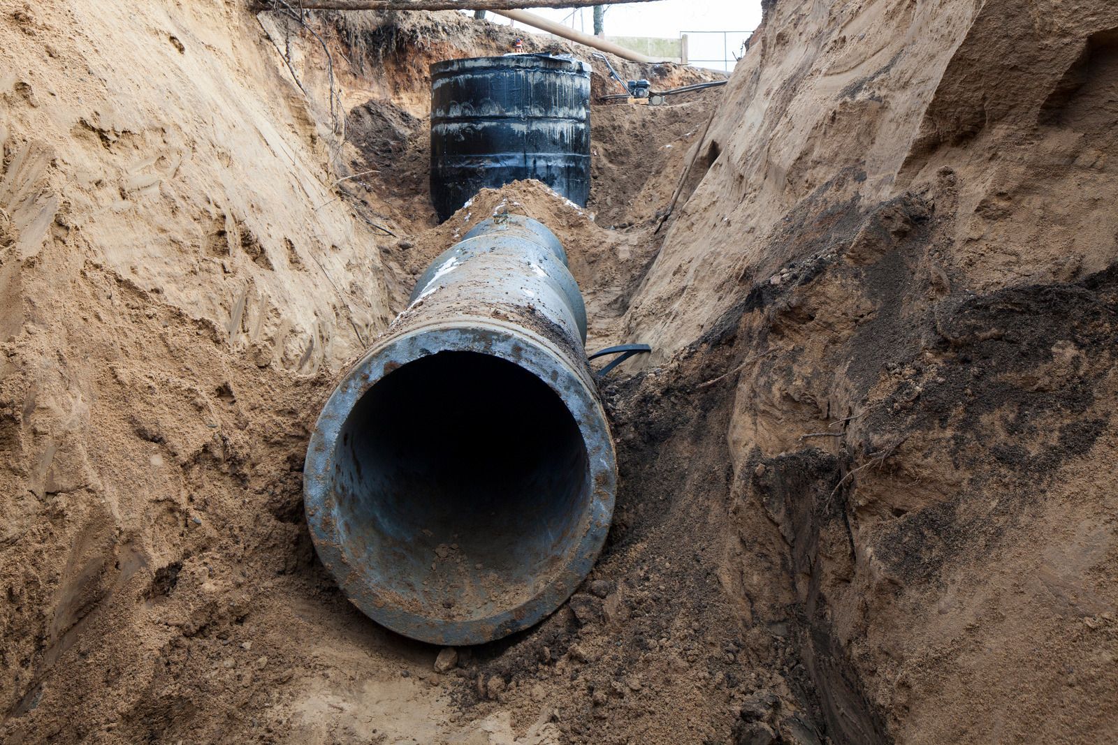 A large pipe is laying in the dirt in a trench.