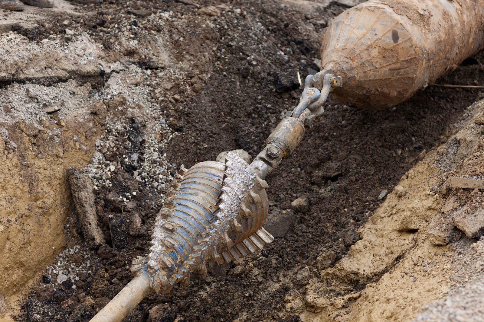 A skeleton is laying in the dirt next to a pipe.