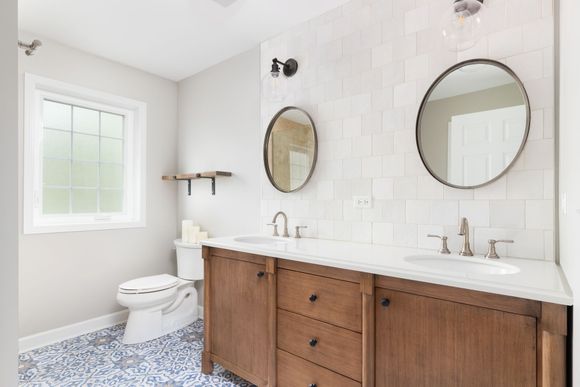 A bathroom with two sinks , a toilet , and two mirrors.