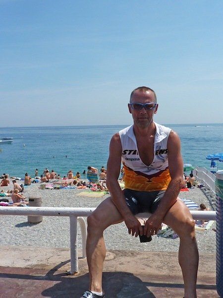 A man is sitting on a railing at the beach with a ktm shirt on
