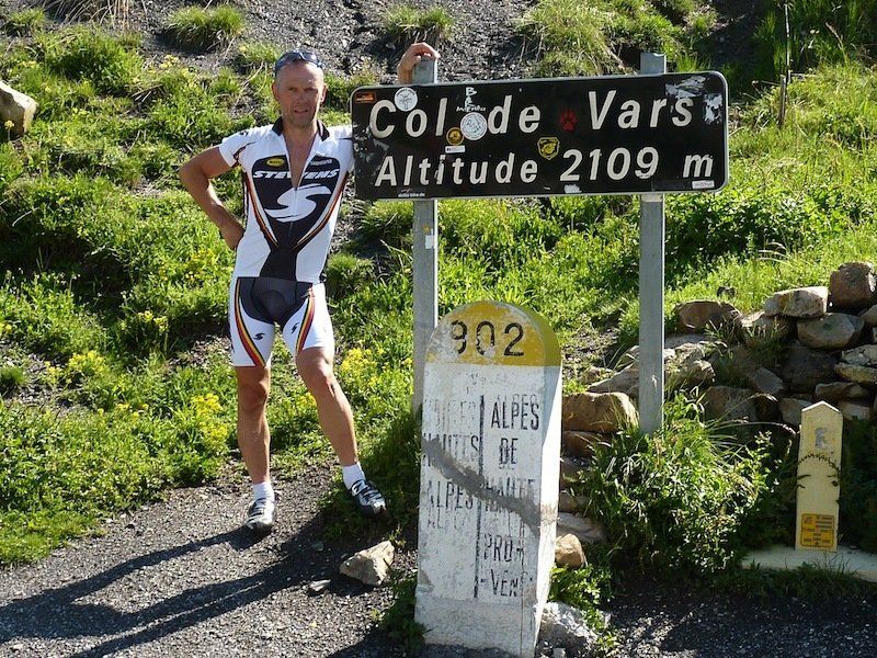 A man stands in front of a sign that says col de vars altitude 2109 m