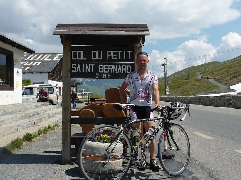 A man standing next to a bicycle in front of a sign that says col du petit saint bernard