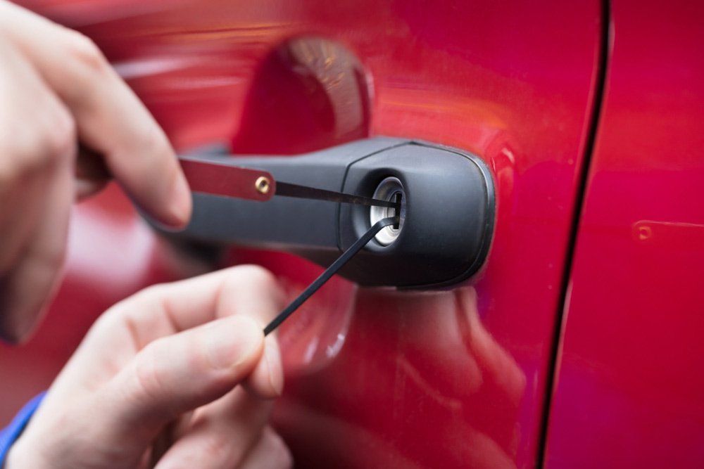 Hand Using Lockpicker Opening Red Locked Car — Locksmith in Newcastle, NSW