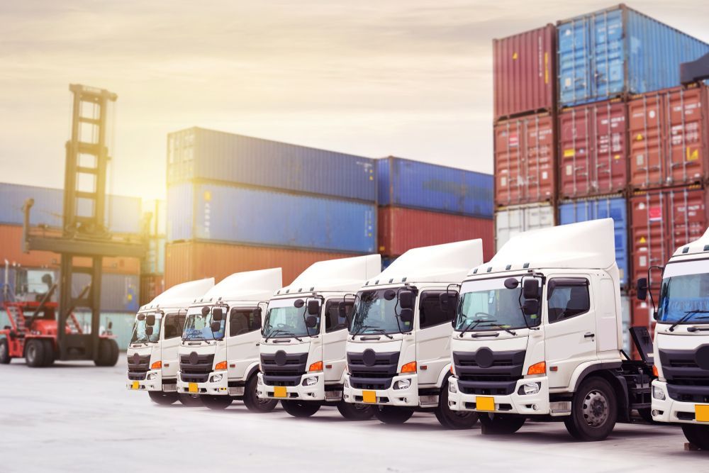 White Trucks Parked at a Shipping Dock With Stacks of Colourful Cargo Containers — Johnny Farming Company In Ooralea, QLD