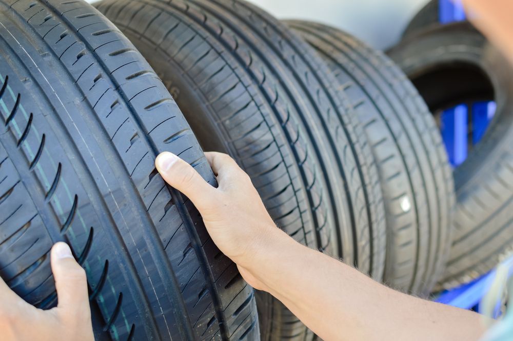 A Person Is Holding A Tire In Their Hands In Front Of A Pile Of Tires — Johnny Farming Company In Ooralea, QLD