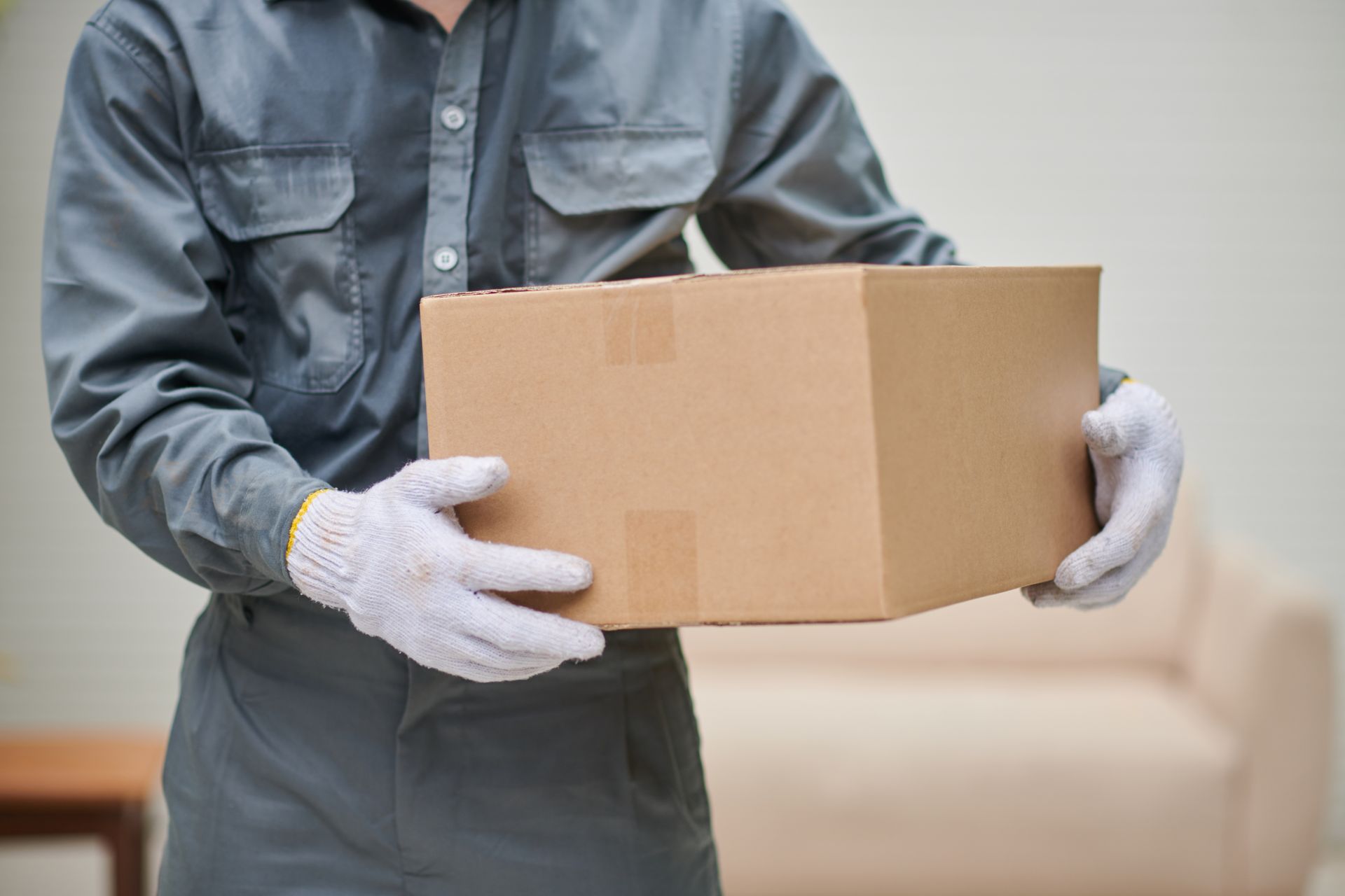 Person in Gray Uniform and White Gloves Holding a Brown Cardboard Box Indoors — Johnny Farming Company In Ooralea, QLD