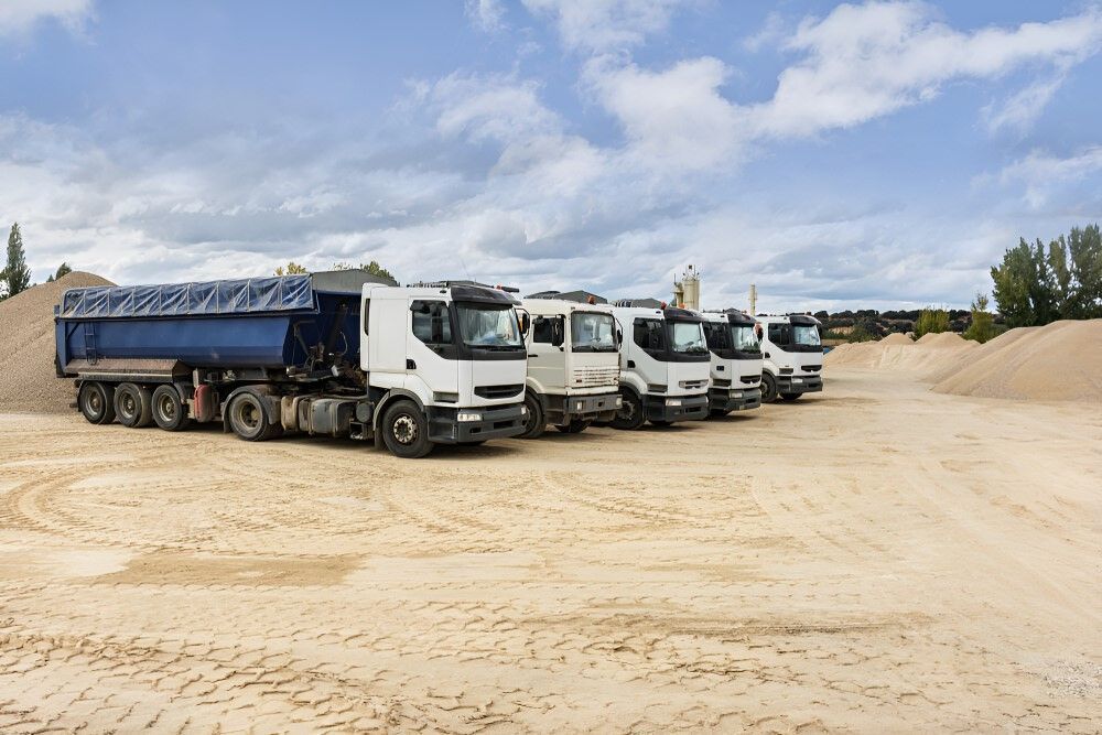 A Row Of Dump Trucks Are Parked In A Dirt Field — Johnny Farming Company In Ooralea, QLD