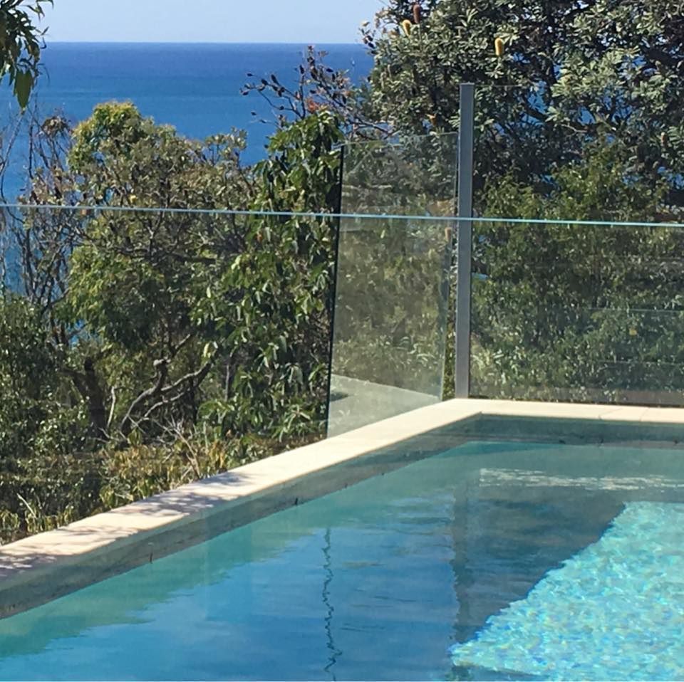 Pool overlooking ocean, surrounded by glass railing and lush trees. Clear water reflects blue sky. — Gympie Fence Inspections in Gympie, QLD