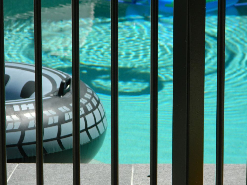 Black and gray inflatable pool float in a turquoise pool, viewed through a black fence. — Gympie Fence Inspections in Rainbow Beach, QLD