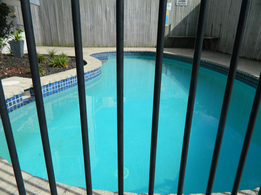 Pool with blue water and tiled edges, viewed through a black metal fence. — Gympie Fence Inspections in Tin Can Bay, QLD
