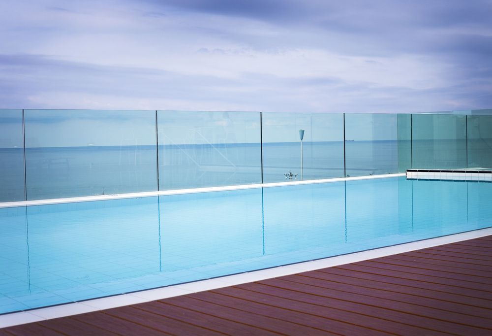 Rooftop pool with glass barriers overlooking a calm ocean under a cloudy sky. — Gympie Fence Inspections in Curra, QLD