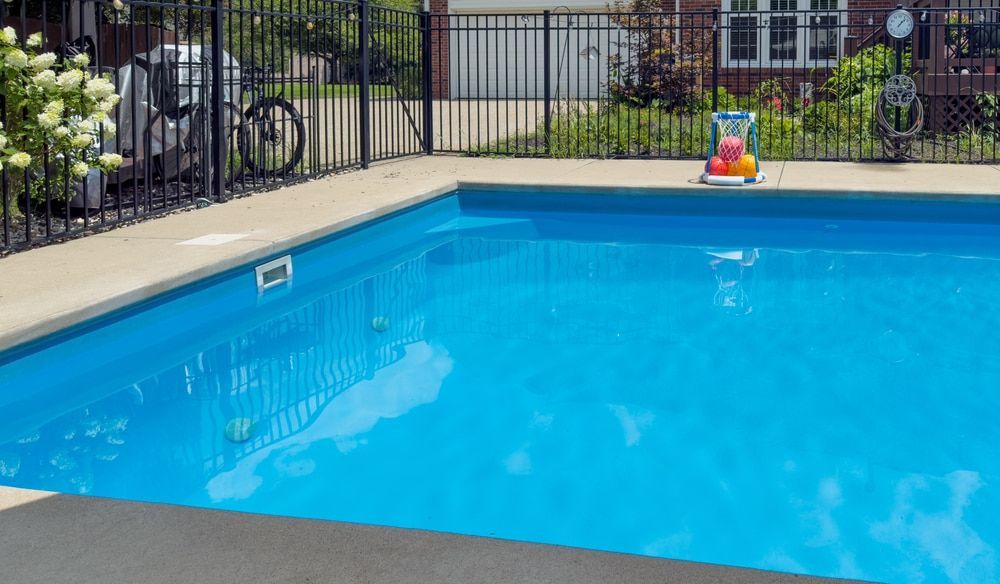 Blue swimming pool with concrete surround, black fence, and small toy. — Gympie Fence Inspections in Kilkivan, QLD
