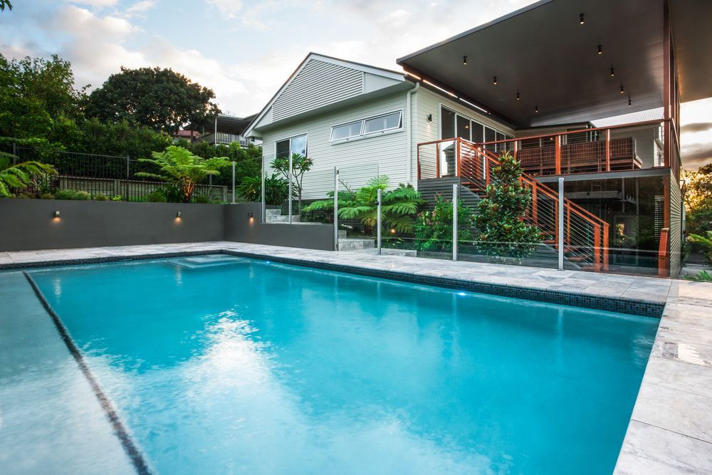 Swimming pool in front of a modern house, with blue water, lush landscaping, and a covered deck. — Gympie Fence Inspections in Curra, QLD