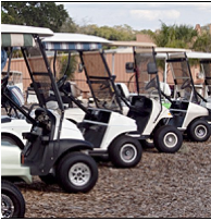 A row of golf carts parked in a gravel lot.