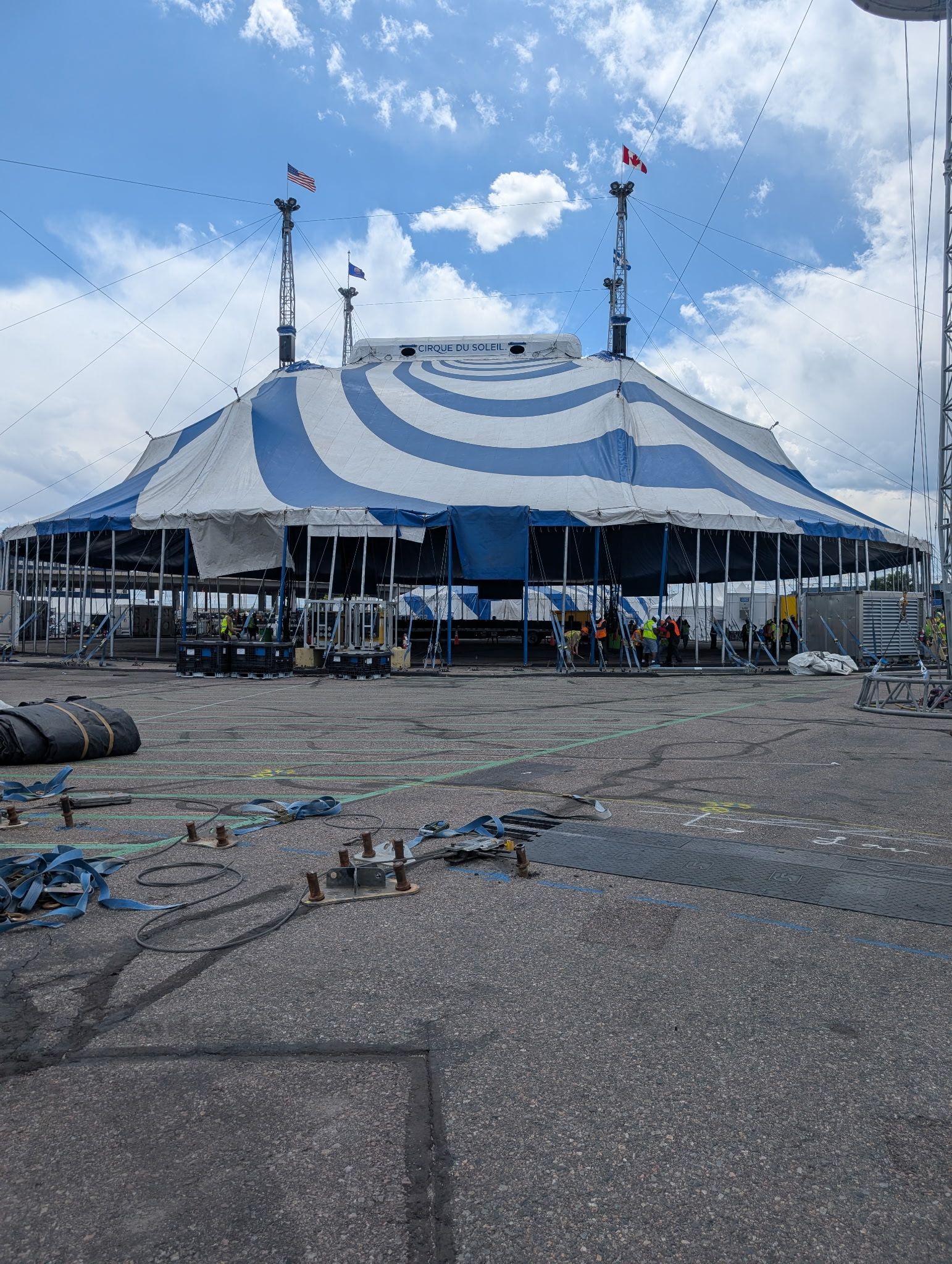 Blue and white striped circus tent set up outdoors on asphalt; rigging and equipment visible.