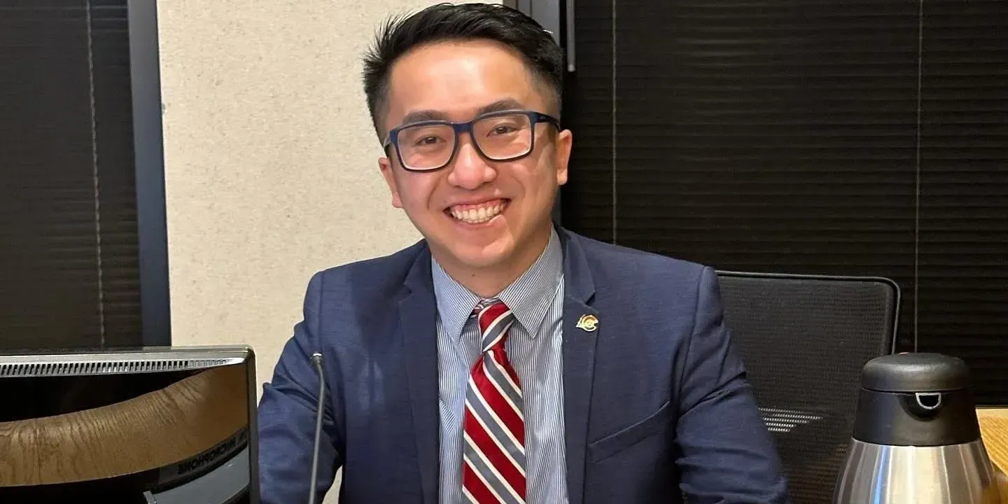 Smiling person in a blue suit and red-striped tie seated at a desk in an office.