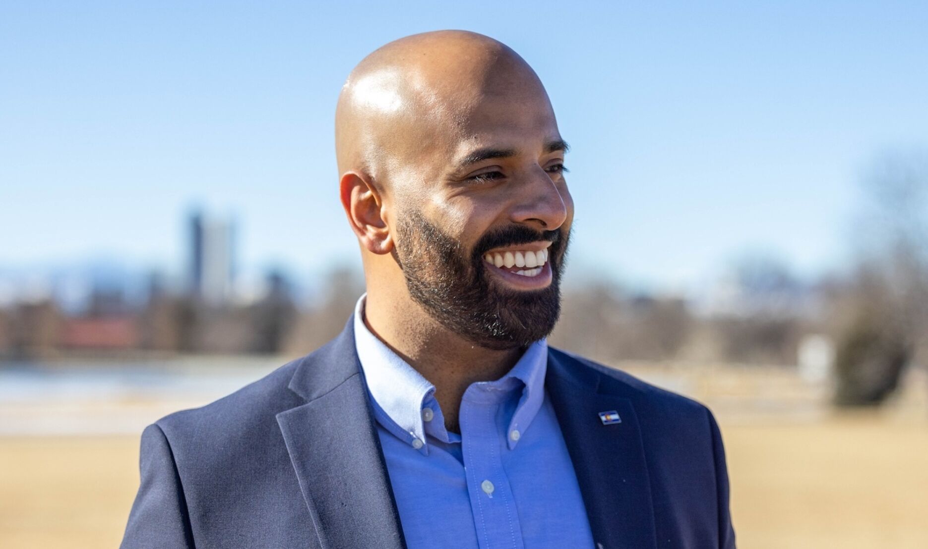 Smiling man in a blue blazer standing outdoors on a sunny day