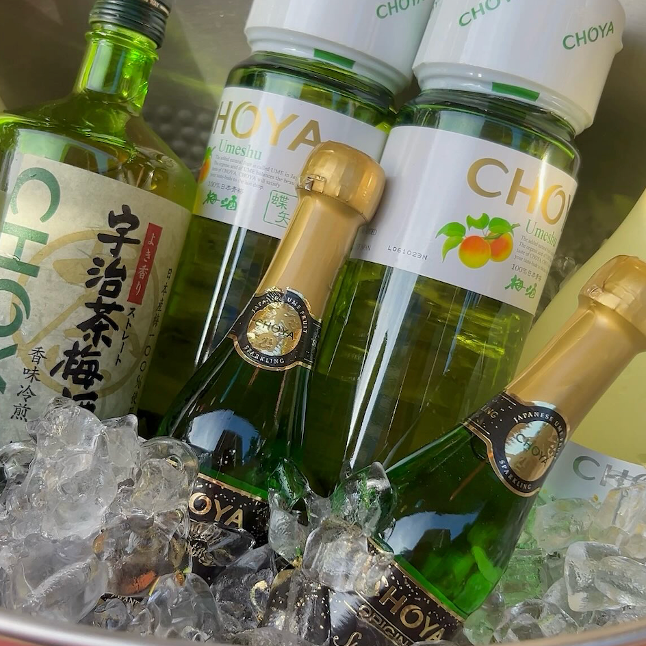 Bottles of Choya Umeshu and sparkling wine chilled in a metal ice bucket.