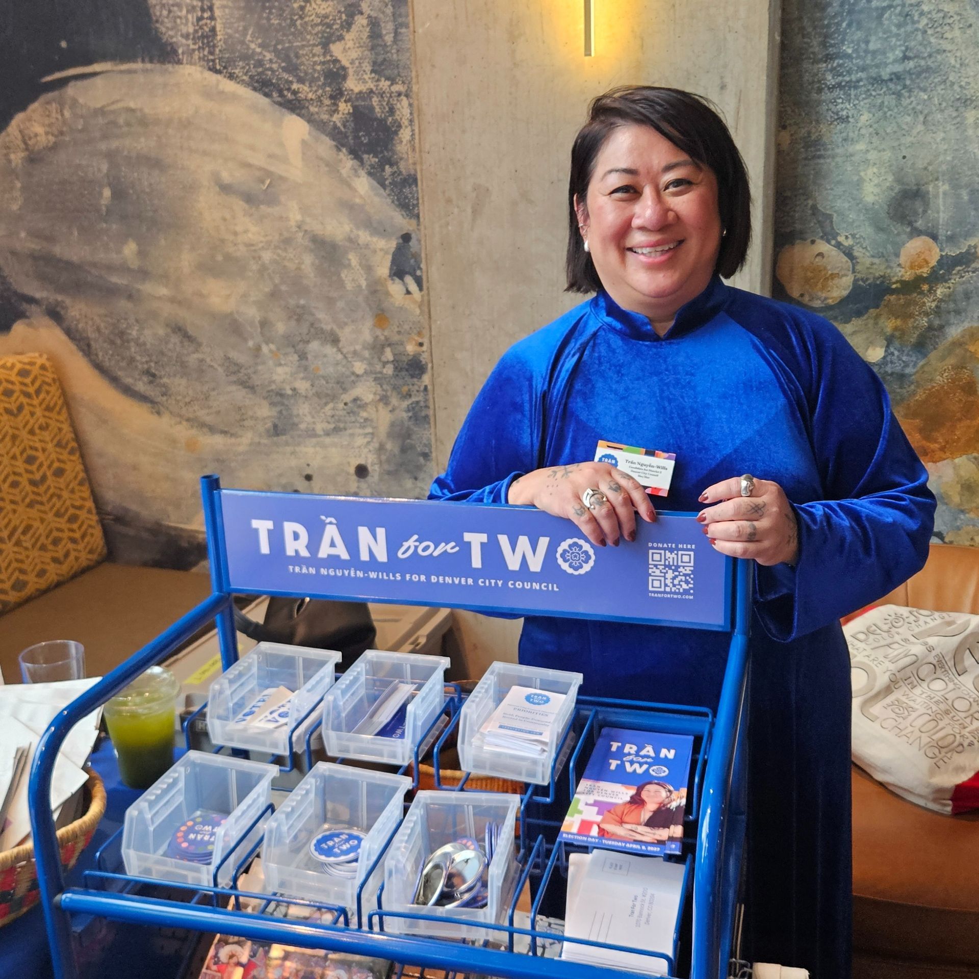 Woman in blue holds a sign behind a raffle box display with clear bins and envelopes