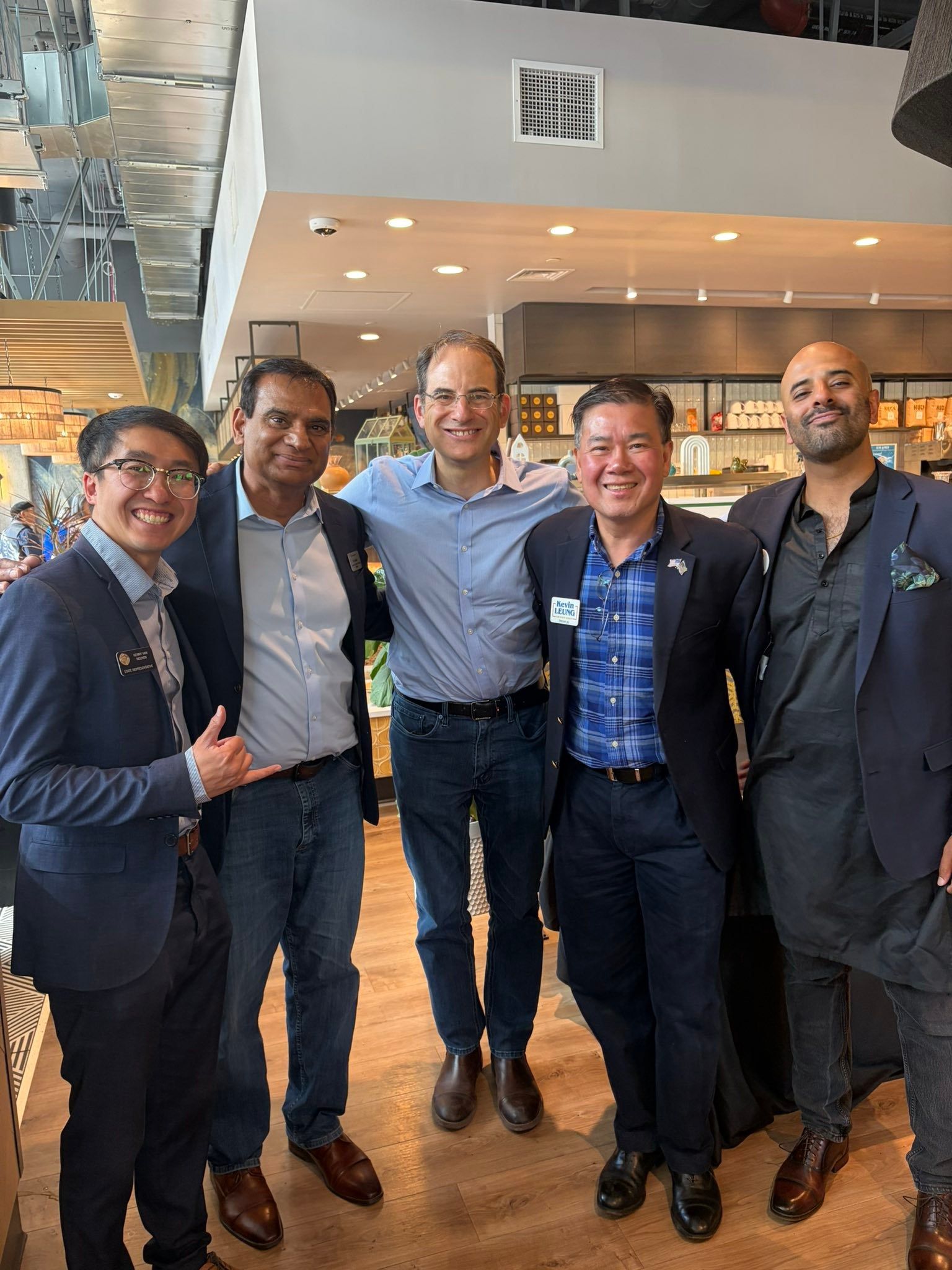 Five men in business attire smiling and posing together in a bright indoor lobby