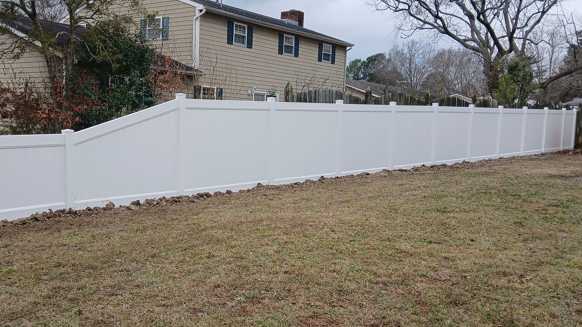 White vinyl fence in a yard, with a two-story house in the background. Brown grass.