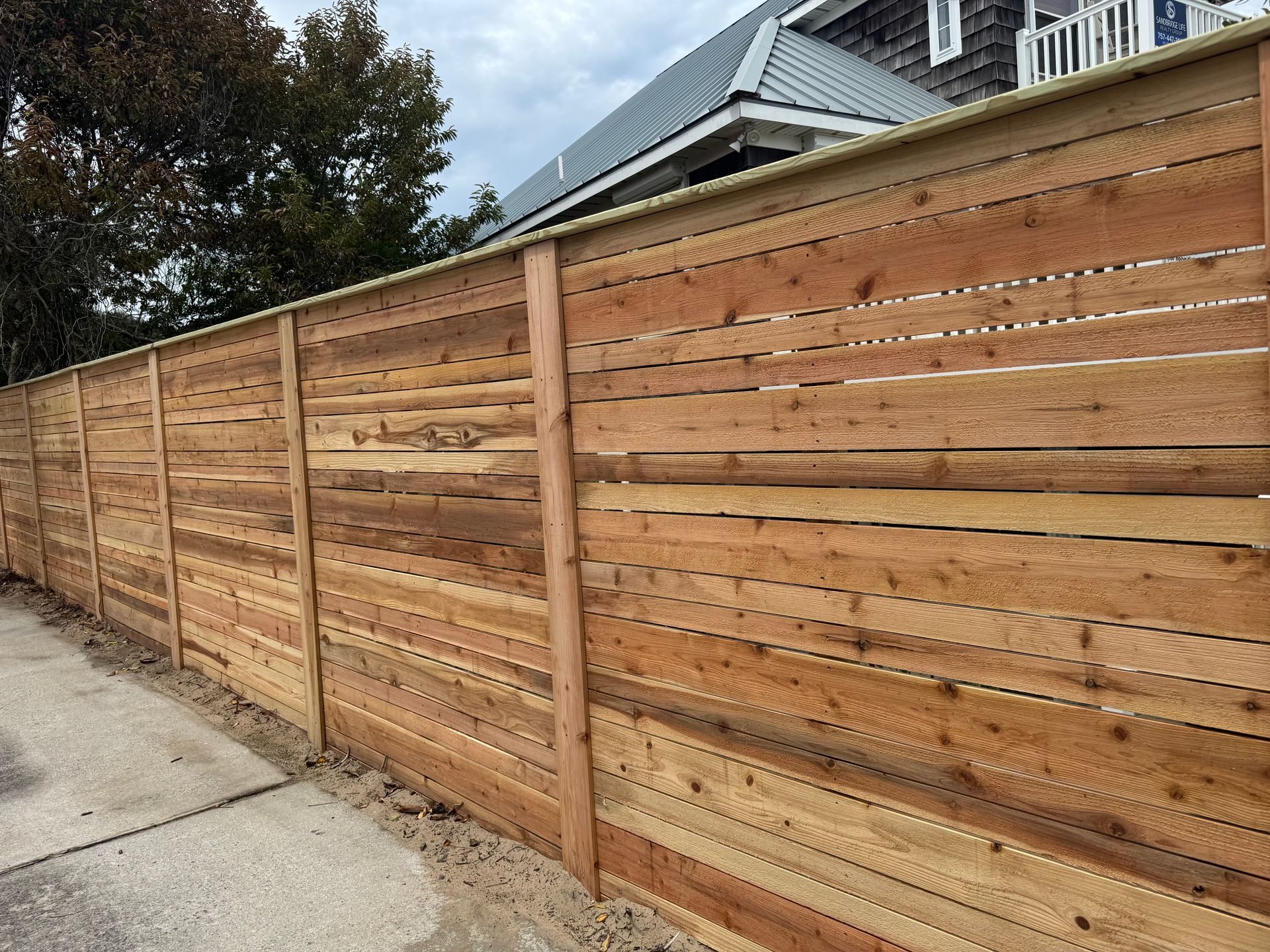 Wooden horizontal slat fence along a sidewalk with a house in the background.