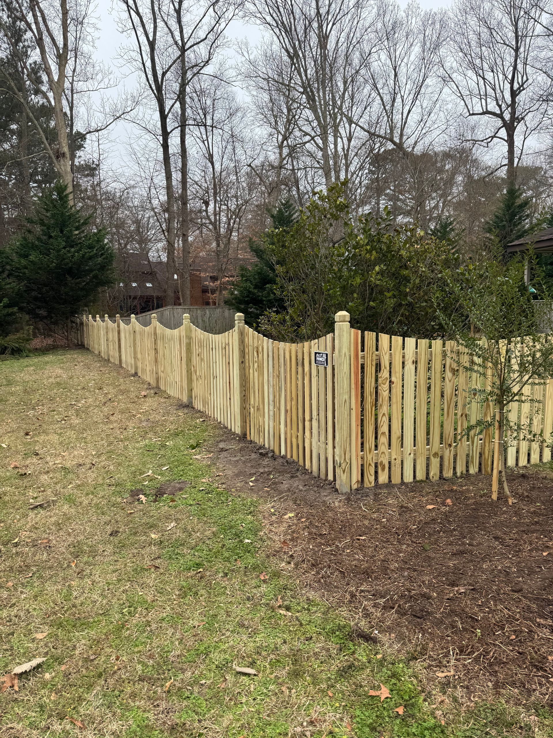 Wooden fence in a yard with trees in the background on a cloudy day.