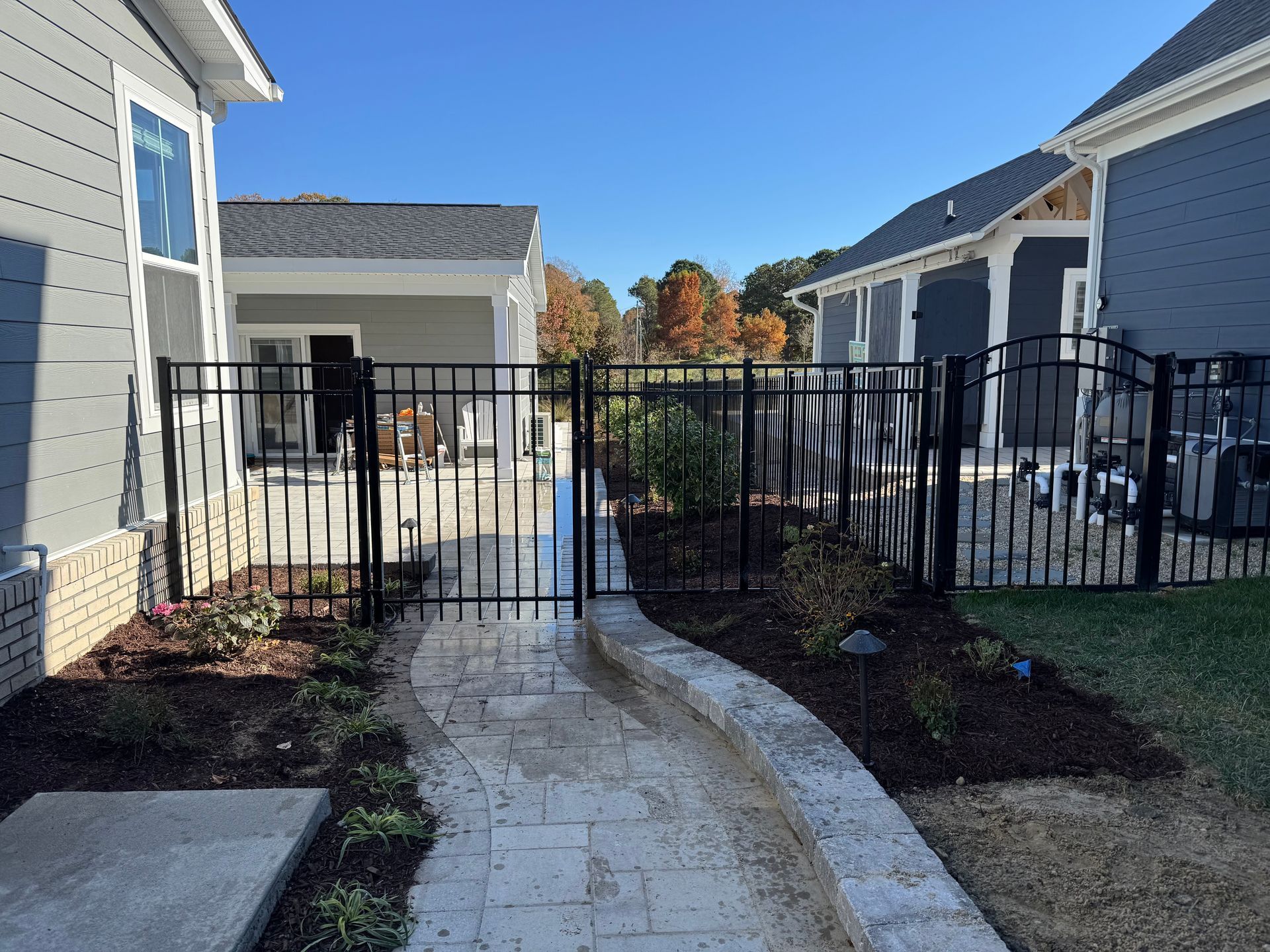 Black metal gate in a pathway between two gray houses with a clear blue sky.